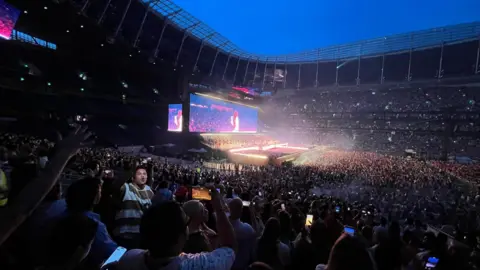 Thousands of fans have their cameras out, taking pictures and videos of the illuminated stage. 