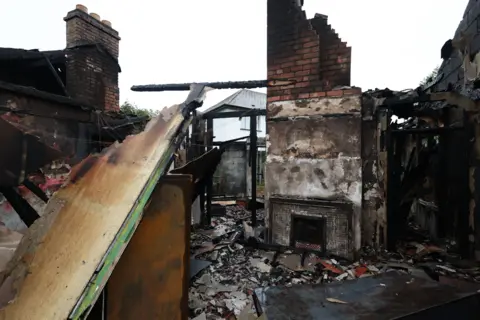 Getty Images A burnt-out house sitting in rubble shows that all that is left is some exterior brick walls, a fireplace and chimney