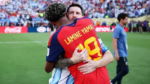 Hector Vivas - FIFA / Getty Images Lionel Messi and Lamine Yamal embrace on the pitch