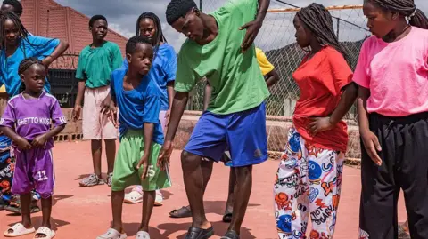 Dancing with Shakira at World Cup was 'very, very, very, very, very good' - Ghetto Kids AFP via Getty Images Members of the Ugandan dance group Ghetto Kids rehearse at their home in Nakawuka, Uganda, on 25 May 2026. They are wearing an array of brightly coloured T-shirts and mimicking the moves of an adult man choreographer.