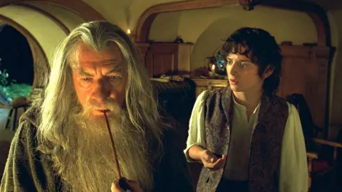 From One Day to One Ring: Leo Woodall joins new The Lord of the Rings cast New Line via Getty Images Ian McKellen on the left is wearing a grey hooded robe holding a smoking pipe to his mouth. He has long grey straight hair and a long grey beard. Elijah on the right is looking at Ian. He has brown curly hair and is wearing a white shirt and open brown waistcoat.