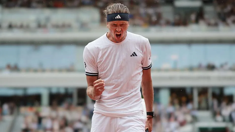 Alexander Zverev, wearing a white t-shirt and black headband, screams with his mouth open and punches his right fist in celebration