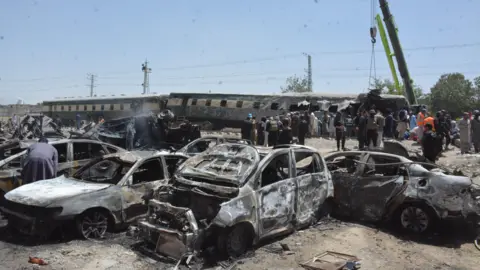 Blast targeting train kills at least 20 in Pakistan Getty Images Burnt-out cars are seen in front of a derailed train, while people stand around.