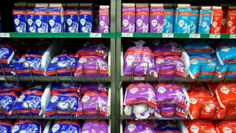Getty Images Shelves of milk, with milk cartons on a top shelf and bags of milk on lower shelves, with different colour packaging - blue, purple or red - representing the fat percentage. 