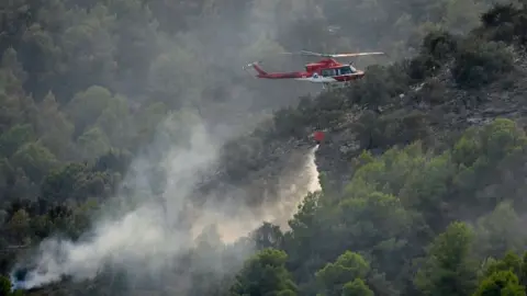 Jose Jordan/AFP via Getty Images A firefighting helicopter dumps water on a wildfire near Betxi, north of Valencia in Spain.