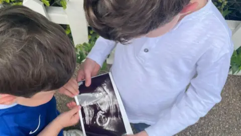 Buckingham Palace Two children look at a picture of a black-and-white baby scan - one boy wears a blue football shirt and the other a pale grey long-sleeved top 