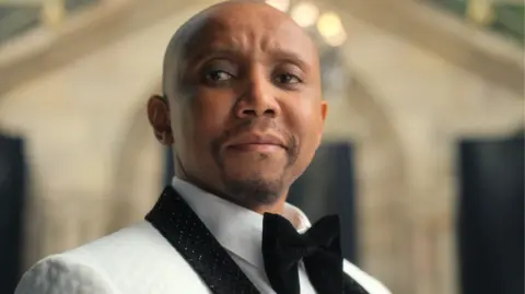 Netflix Actor Sdumo Mtshali in a smart white jacket with black diamante collar and large black velvet bow tie.