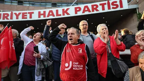 Turkish opposition fights court ousting of leaders in ruling boosting Erdoğan AFP via Getty Images Men and women in red bibs stand outside the headquarters of Turkey's Republican People's Party