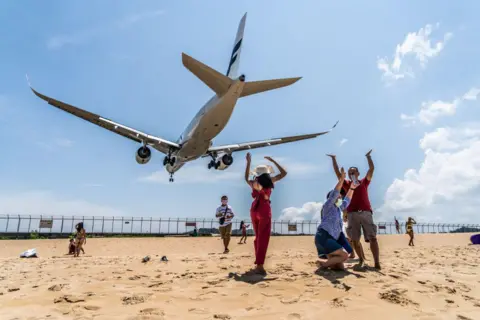 /LightRocket via Getty Images Tourists celebrate at Mai Khao beach as a Finnair jet from Helsinki lands at Phuket International Airport. 