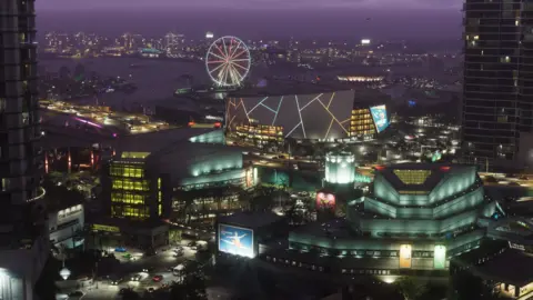 GTA 6 leaks - a nightmare or a blip for the biggest video game of the year? Rockstar Games An aerial screenshot shows downtown Vice City at night. Blocks of apartments, a stadium with a large animated billboard and an illuminated Ferris wheel create a glowing tapestry of colours. In the distance, on the other side of a port, the lights of more buildings dot the skyline.