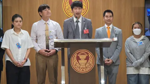 The BTS fans losing thousands as scammers cash in on comeback tour 'ticket war' Supplied by Juraluk Kunaruk Juraluk Kunaruk (first from right), standing before the Thai parliament as MP Nitikorn Bunyakulcharoen (centre) addresses lawmakers on the spate of scams around BTS concert tickets