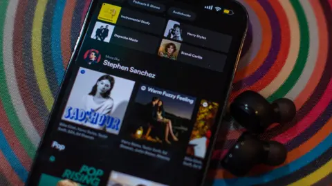 Why Spotify has no button to filter out AI music Getty Images A phone showing the Spotify app with various musicians