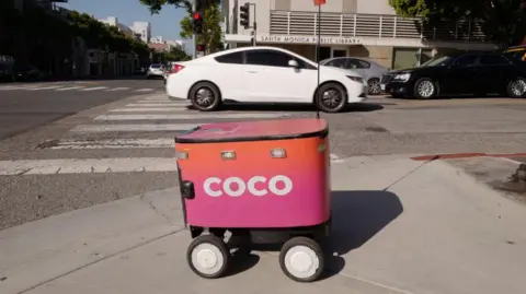 Coco A delivery robot in front of a car on a street in Los Angeles