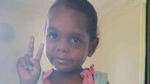 Man charged with murder and sexual assault of 5-year-old Australian girl Northern Territory Police An Aboriginal girl wearing a pink dress and blue backpack poses for a picture, holding up the peace sign