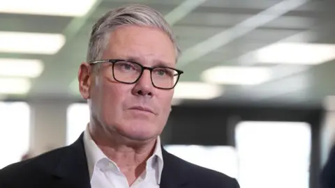 PA Media Sir Keir Starmer, who has grey short hair styled in a side parting and wears thin-rimmed glasses, a white shirt and black suit jacket, looks serious