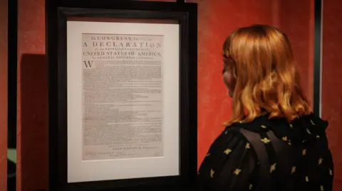 Crown Copyright/The National Archives A woman with red hair looks at a framed copy of the Declaration of Independence in a brightly-lit room.