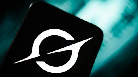 Getty Images An image of the white Grok logo on a smartphone in front of a teal coloured blurred abstract background.