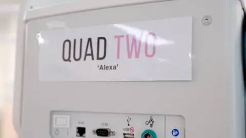 Metro North Health The side of a baby incubator with a laminated sign attached to it that reads 'Quad Two 'Alexa''