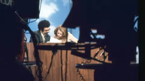 Raimondo Borea/Gartenberg Media Enterprises/Getty Images View, between TV cameras, of journalists Gene Shalit and Barbara Walters on the 'Today Show' set at NBC Studios, New York, New York, mid 1970s. 

