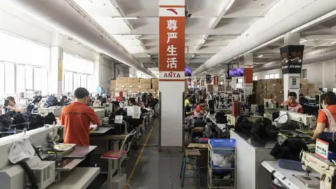 Getty Images A sign in Chinese characters reading "Dignified Living" is displayed on a pillar in a shoe production line at an Anta factory in Jinjiang.