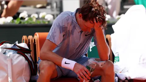 EPA Jannik Sinner holds his head in one hand as he drinks water in the heat during a break at the French Open.