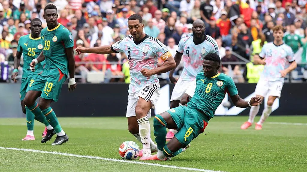 First Afcon, now World Cup - Senegal trapped in 'football hell' Belgium captain Youri Tielemans is fouled by Lamine Camara during the 2026 World Cup last-32 tie in Seattle. Tielemans is standing with his left leg planted forward as Camara slides in from the side, leading with his right leg. The contact between the pair is difficult to see, with the ball positioned right in front of their pink boots. Behind them, watching on, are two Senegal defenders and two Belgium attackers, including Romelu Lukaku. The Belgians wear white socks and shorts and light shirts made up of pink and turquoise patches, while the Senegalese are all in green with red and yellow trim. A blurred section of crowd is visible in the background