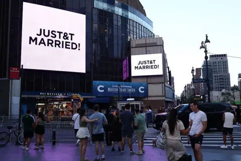 Taylor Swift and Travis Kelce wed in NYC in ceremony officiated by Adam Sandler Getty Images People watch giant screens showing the message "JUST&T MARRIED!" (T&T for Taylor and Travis) outside Madison Square Garden, the reported venue for the wedding celebrations of pop singer Taylor Swift and pro-athlete Travis Kelce.