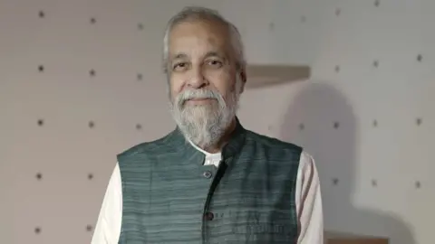 Instagram running ads promoting child sexual abuse material in India, BBC finds Madan Lokur is stood in a room with white walls, looking at the camera. He is wearing a sleeveless jacket over a white top and has grey hair and a grey beard.