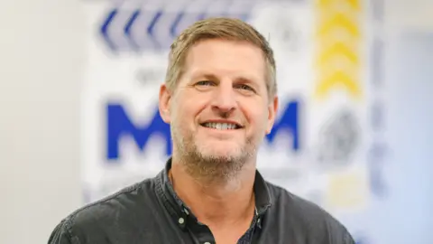 Businesses scramble to get noticed by AI search Jamie Akrill/MKM Building Supplies Andy Pickup wearing a black shirt, with a button-down collar.