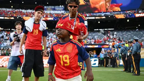 Hannah Peters - FIFA / Getty Images Keyne wears a number 19 shirt and a cap partially covering his eyes. His brother is behind him