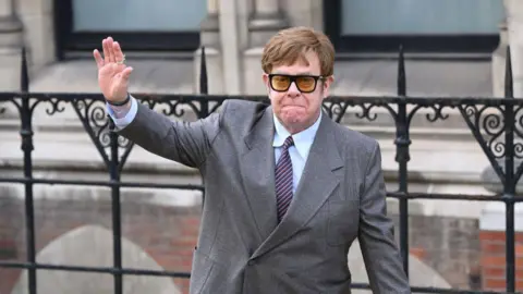 Getty Images Sir Elton John in a suit, tie and sunglasses, waving outside the Royal Courts of Justice in 2023
