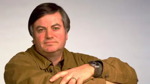 Getty Images Journalist Roger Cook wearing a khaki shirt with is arms folded, looking at the camera.