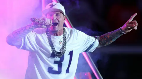 Multiple artists drop out of US Freedom 250 concert Getty Images Vanilla Ice sings into a microphone He wears a white NFL jersey with the number 31 on the front, a white baseball cap and a big silver neck chain.