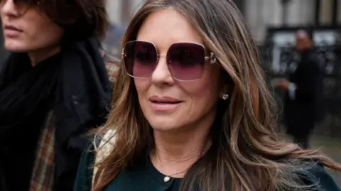 PA Media Elizabeth Hurley, in a green outfit and sunglasses, leaves the Royal Courts of Justice 