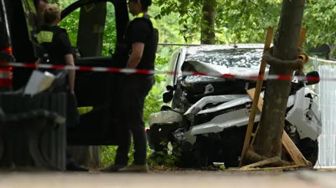 Reuters A white van is pictured crashed into a tree with police standing next to a car nearby