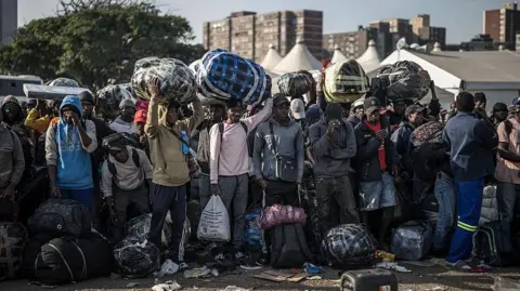 AFP via Getty Images Migrants lining up near a bus to take them away