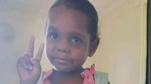 Violence in Australian town after arrest of man over girl's murder Northern Territory Police An girl wearing a pink dress and blue backpack poses for a picture, holding up the peace sign