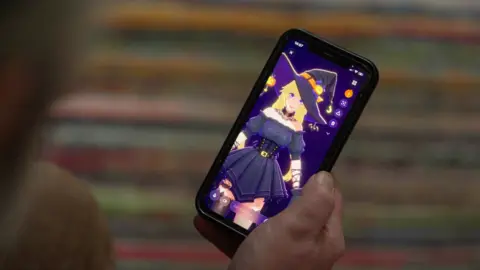 A person holds a phone showing a character on the app called Ani