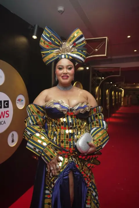 Dress made from 500 loaves stuns Africa Magic Viewers' Choice Awards BBC/GIFT UFUOMA Reality TV star, OJ Posharella graces the red carpet with a giant bow sitting on her head as she stuns in her multi-layered colorful outfit she designed herself.