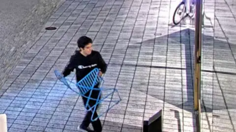 Man faces attempted murder charges in attack on home of OpenAI's Sam Altman US Justice Dpeartment Man with black hair in black sweatsuit lifts blue-colored folding chair while walking outside toward a glass door