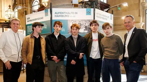 Getty Images Steve Rotheram, actors Rhys Mannion, actor Harvey Brett, actor Patrick Gilmore, actor and musician Ellis Murphy, actor Louis Landau and Hamburg's State Secretary of the Ministry of the Interior and Sports, Christoph Holstein pose for a photo during the opening of the exhibition "Hafenstaedte. Schaupaetze der Welt" at Hamburg City Hall 
