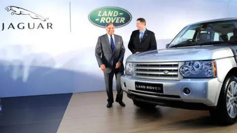 AFP via Getty Images Tata Group's Ratan Tata and then Land Rover Managing Director Phil Popham pictured in front of a Land Rover car with the Jaguar and Land Rover logos in the backdrop, at an event in Mumbai in 2009. 