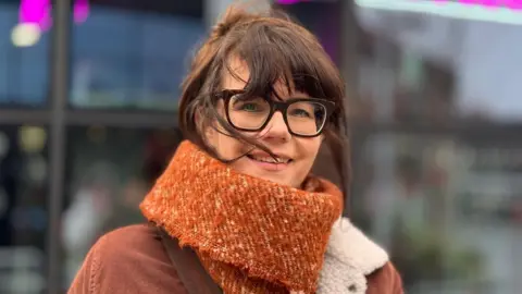 Businesses scramble to get noticed by AI search Lyn Lowe Ann Lowe wears glasses and a large, dark orange scarf.