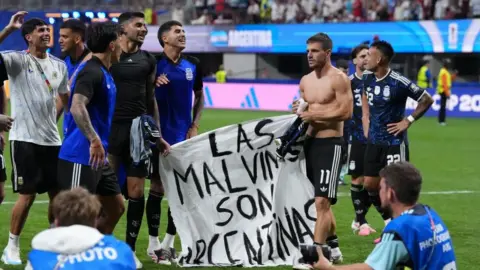 PA Media Several Argentinian football players standing on a pitch holding a banner saying "Las Malvinas Son Argentinas"