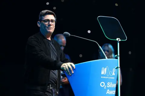Getty Images Andy Burnham speaks at a podium during the Silver Clef Awards