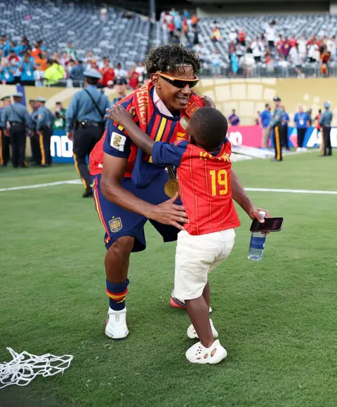Maja Hitij - FIFA / Getty Images Keyne is seen extending his arms out as his older brother Yamal leans down to pick him up