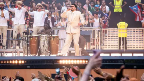 Getty Images Bad Bunny on stage with musicians as members of the crowd behind him and in front of him watch and wave their hands