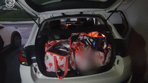 NSW Police Force Several red and white bags with apples on them in the boot of a white car.