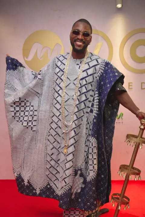 Dress made from 500 loaves stuns Africa Magic Viewers' Choice Awards BBC/GIFT UFUOMA Tobi Bakre is dressed in a traditional outfit and is carrying a brass staff