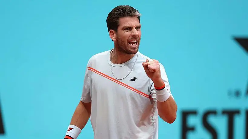 Gauff beats Cirstea in Madrid despite stomach virus Cameron Norrie is wearing a white t-shirt with an orange sash and holding up his fist